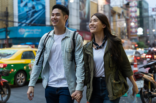 Asian active young couple travel in city for honeymoon trip at night. Attractive new marriage man and woman backpacker tourist walking on street enjoy spend time dating on valentines vacation together