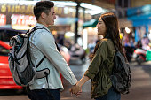 アジアの活発な若いカップルは、夜に新婚旅行旅行のために街で旅行します。魅力的な新しい結婚の男性と女性のバックパッカー観光客が通りを歩いて、一緒にバレンタイン休暇でデートす�
