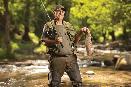 Pescador maduro sonriente sosteniendo un pez carpa y de pie en un río photo