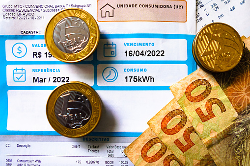 19 de mayo de 2022, Brasil. Una factura de electricidad (electricidad), que indica el consumo mensual de 175 kilovatios-hora (kWh), con billetes y monedas del Real Brasileño. photo