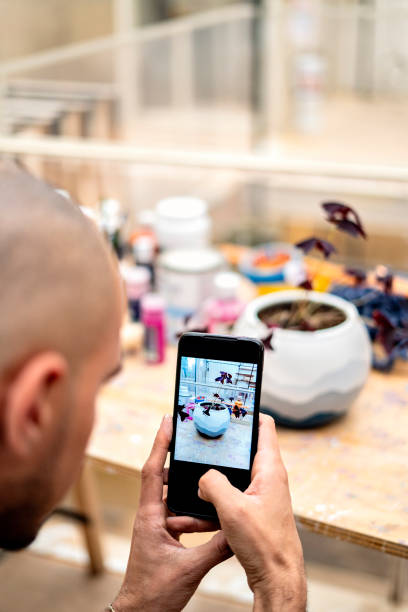 istock Man photographing a flower pot on a table with his cell phone. 1398212575
