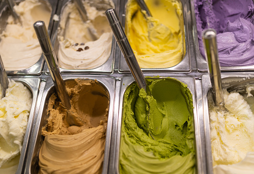 A close up of various colors and flavors of ice cream in an ice cream shop on offer.