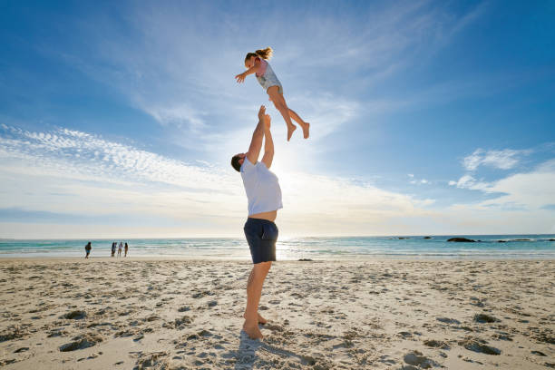 istock Father lifting daughter, having fun on the beach. A smiling young man playing with his cute little girl on vacation. Fun family vacation 1398217801