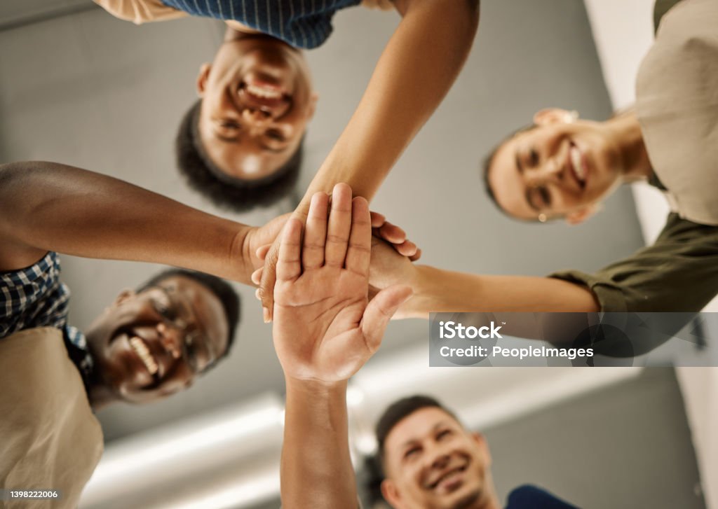 Diverse businesspeople hands stacked from below. Group of fashion designers celebrating and motivating each other. Tailors huddled with hands piled. Group of designers having fun with hands stacked Directly Below Stock Photo