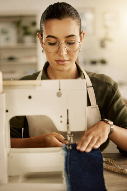 istock Mixed race designer sewing a piece of denim. Young tailor using a sewing machine. Creative businesswoman stitching a piece of fabric. Fashion designer sewing a piece of material 1398222913