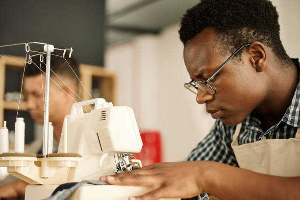 istock Focused designer sewing fabric. Focused tailor using sewing machine. African American designer sewing a piece of denim. Young businessman working on a sewing machine. Tailor sewing a garment 1398222935