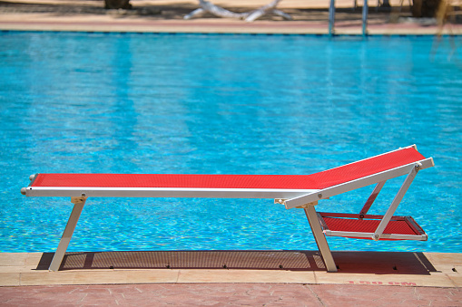 Empty deck chair on swimming pool side in summer resort. Vacations and getaway concept.
