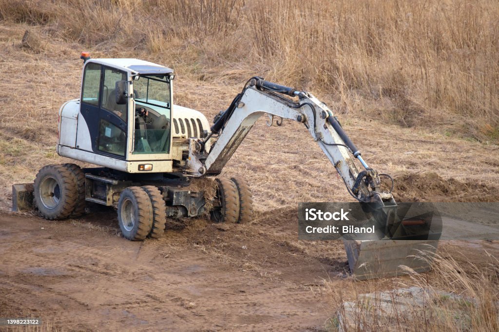 Earth moving tractor preparing place for future house foundation construction. Leveling soil for building new home Earth moving tractor preparing place for future house foundation construction. Leveling soil for building new home. Backhoe Stock Photo
