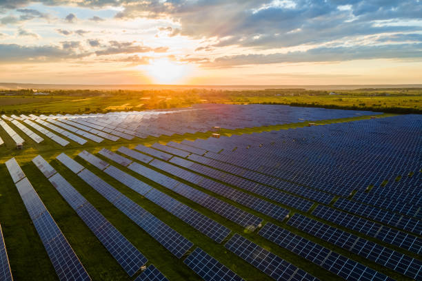 日没時にクリーンな電気エネルギーを生産するための太陽光発電パネルの多くの列を持つ大規模な持続可能な発電所の空中写真。ゼロエミッションコンセプトの再生可能電力。 - インダストリアル音楽 ストックフォトと画像