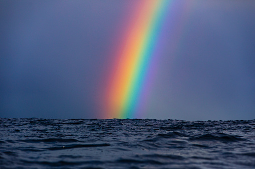 Bright vivid rainbow against stormy background at surface level in the open ocean