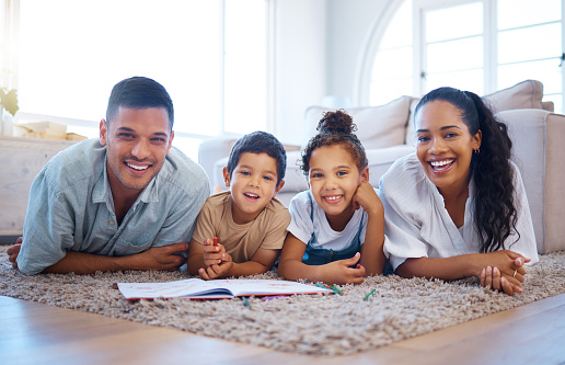 Portrait of a smiling young mixed race family lying close together on the living room floor at home. Happy adorable hispanic son and daughter bonding with their mother and father during a weekend