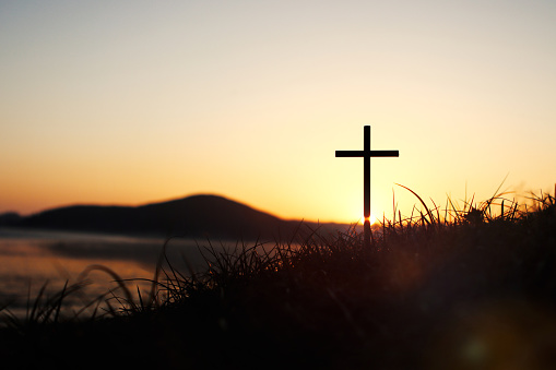 The holy cross of Jesus Christ on the grass with the strong light of the sunset sky symbolizes death and resurrection love.