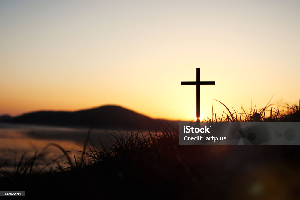 The holy cross of Jesus Christ on the grass with a strong light in the sunset sky The holy cross of Jesus Christ on the grass with the strong light of the sunset sky symbolizes death and resurrection love. Religious Cross Stock Photo