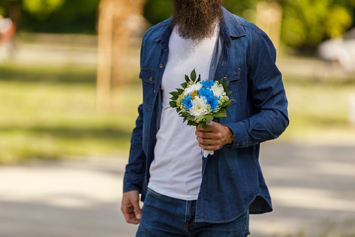 Midsection of unrecognizable young man standing on the street at the park, holding a a beautiful bouquet of flowers when waiting to meet his girlfriend.