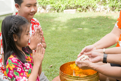 Happy Asian Family with children pouring water on hands of parent for respected as Thai New years at outdoors of the house, Tradition of Thai Religious blessing culture. Thai Family day at April of every years.