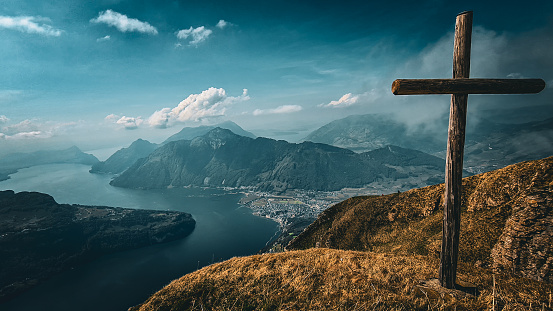A cross on the top of the mountain with a view to the Lake Lucern and other mountains on a cloudy day.