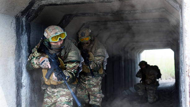 istock Three military mercenaries walk against a concrete wall background and smoke. Collage - one model in three poses. Photo format 16x9. 1398241613