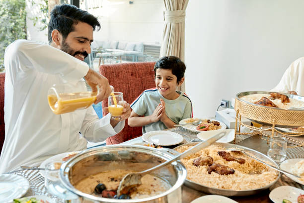 pai do oriente médio servindo suco de frutas para filho sorridente - saudi arabia child ramadan offspring - fotografias e filmes do acervo