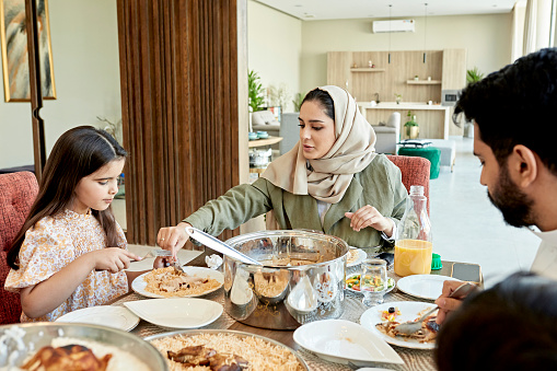 Joven madre saudí sirviendo a su hija en la mesa del comedor photo