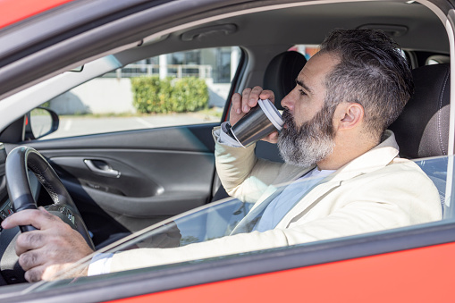 Mature man drinking coffee to go when driving a car