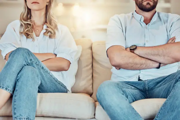 Photo of Unknown couple fighting and giving each other the silent treatment. Caucasian man and woman sitting on the sofa with their arms folded after an argument. Unhappy husband and wife ignoring each other