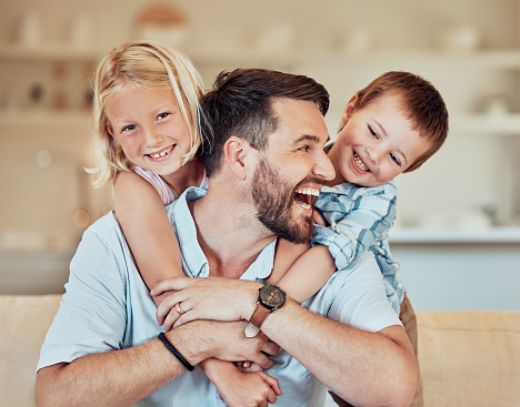 Young happy cheerful caucasian father spending time with his son and daughter at home. Little brother and sister hugging their dad together. Family relaxing and bonding at home