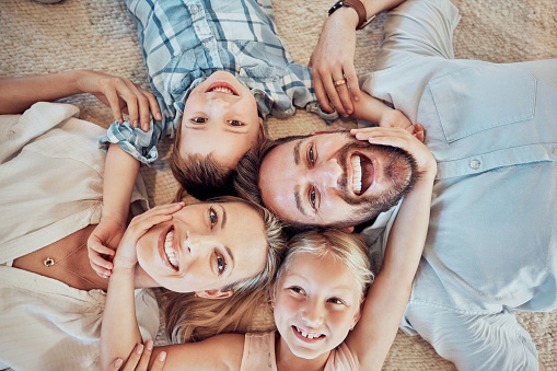 Above view of young family lying on the floor in a circle and taking selfies. Portrait of happy parents bonding with their son and daughter at home. Adorable smiling siblings enjoying free time inside