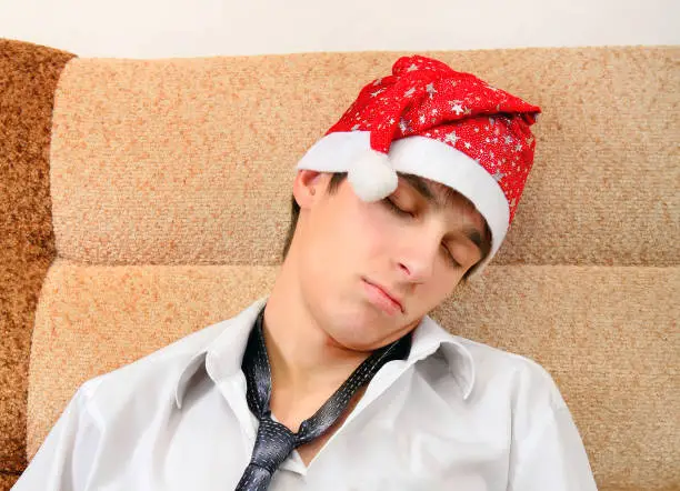 Tired Young Man in Santa Hat sleep on the Sofa at the Home