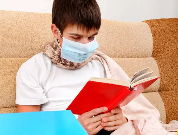 Sick Teenager in Flu Mask read a Book on the Sofa at the Home