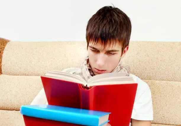 Young Man reads a Books on the Sofa at the Home