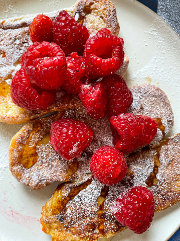 Stock photo showing close-up, elevated view of brioche, homemade eggy bread often called French toast on white plate.