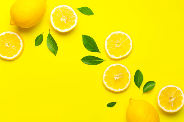 istock Creative background with fresh lemons and green leaves on bright yellow background. Top view flat lay copy space. Lemon fruit citrus minimal concept vitamin C. Composition with whole, slices of lemons 1398249466