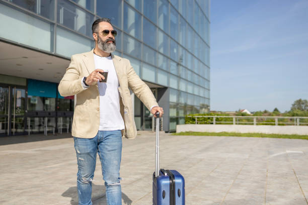 istock Handsome man holding coffee to go and pulling suitcase from airport 1398249548