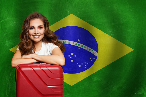 Love Brazil. Attractive woman with red suitcase on Brazilian flag background. Travel, work, education and internship in Brazil