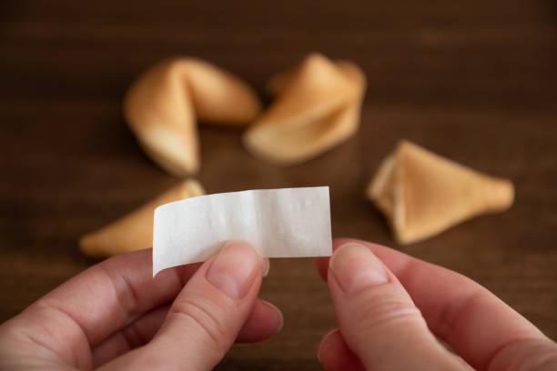 la persona sostiene en las manos papel en blanco de la galleta de la fortuna contra unas pocas galletas que yacen sobre el fondo de la superficie de la mesa, maqueta para su deseo de buena suerte - luck fortune telling cookie fortune cookie fotografías e imágenes de stock