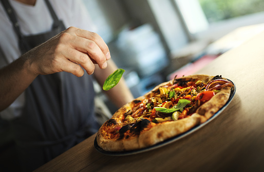Closeup side view of a chef putting some basil leaves on top of a freshly baked pizza.
