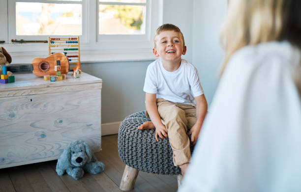 un adorable petit garçon assis sur une chaise tout en parlant à un thérapeute caucasien. mignon petit garçon parlant à un psychologue. l’enfant consulte un conseiller dans un foyer d’accueil avant d’être adopté - child therapy photos et images de collection