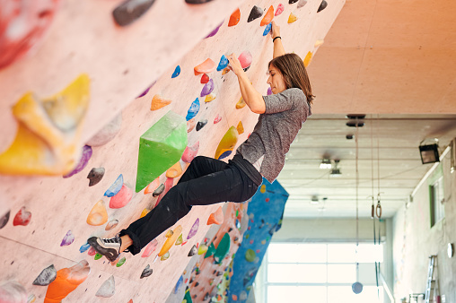 Side view of focused female climber ascending angled wall during boulder workout in sunlit gym