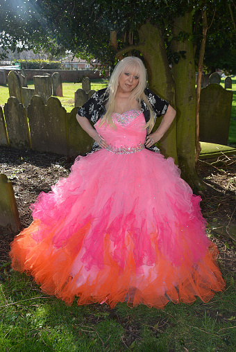 Mature female model wearing a pink evening dress while standing under a large tree in an outdoor location