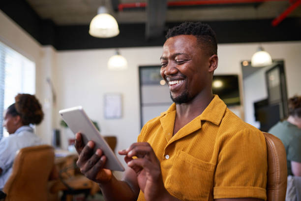A Black man uses a digital tablet in the open-plan office wearing bright shirt