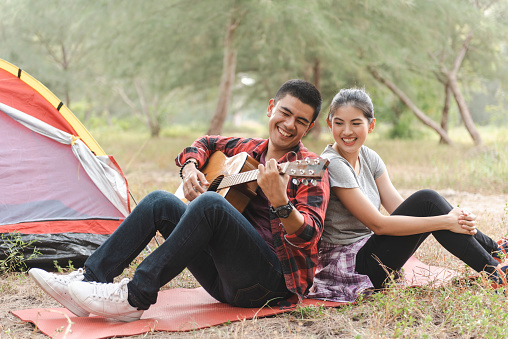 Asian couple singing and playing guitar near the forest tent