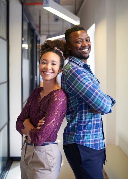 Two co-founders stand back to back with arms crossed in office corridor