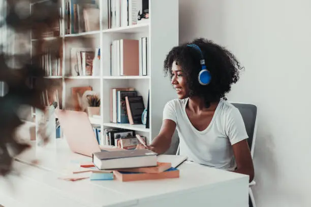 Photo of Young woman working on laptop with headphone at home in living room.