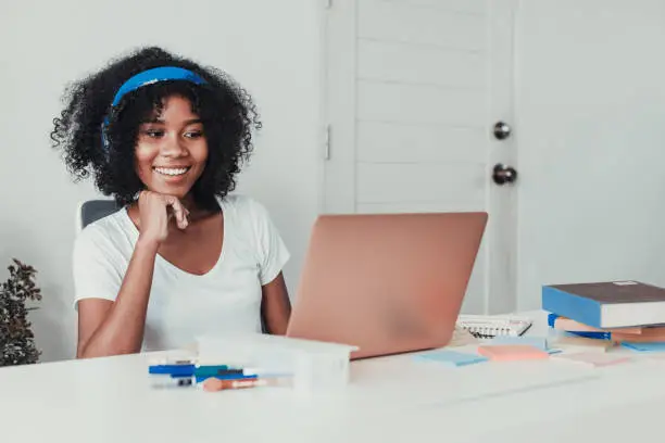 Photo of Young woman working on laptop with headphone at home in living room.