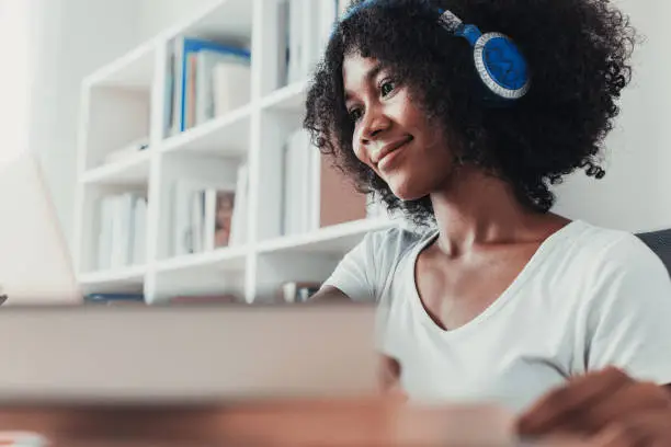 Photo of Young woman working on laptop with headphone at home in living room.