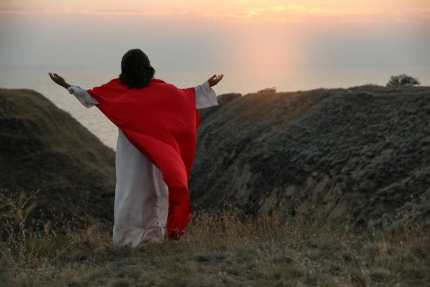 istock Jesus Christ raising hands on hills at sunset, back view. Space for text 1398266797