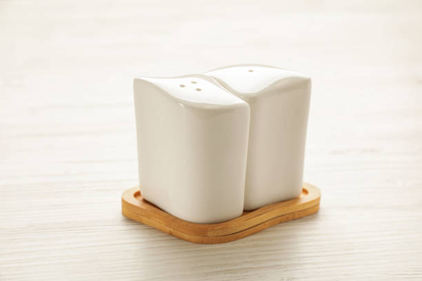 Ceramic salt and pepper shakers with stand on white wooden table, closeup