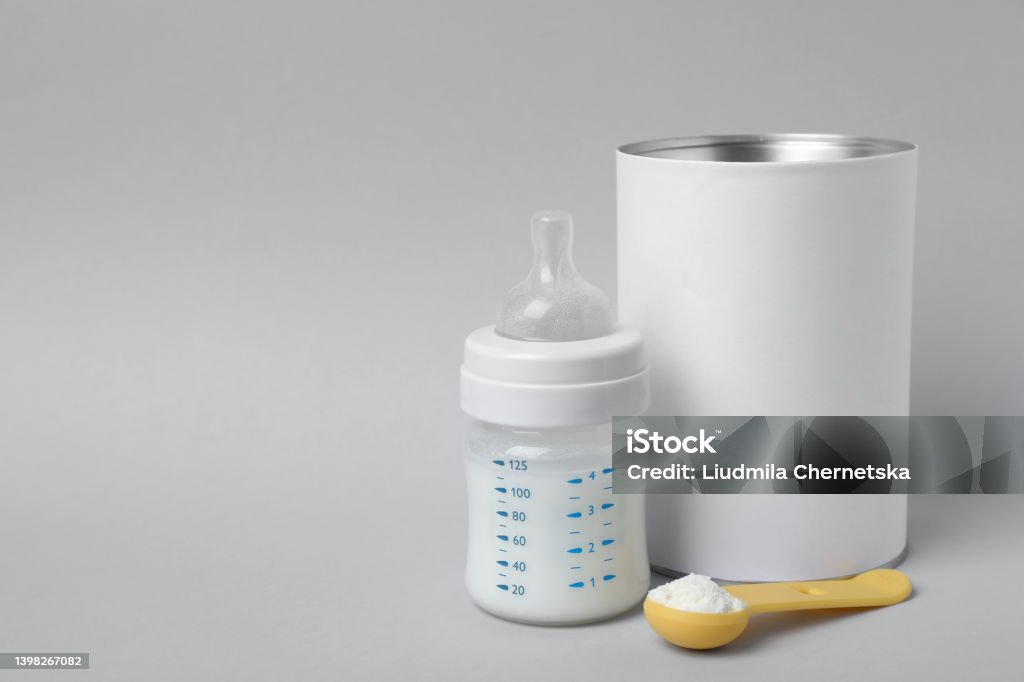 Blank can of powdered infant formula with scoop and feeding bottle on light grey background, space for text. Baby milk Infant Formula Stock Photo