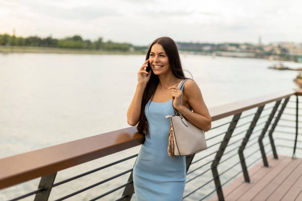 istock Young woman using a mobile phone while walking on the river promenade 1398267086