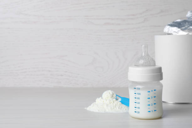 istock Powdered infant formula, scoop and feeding bottle on white wooden table, space for text. Baby milk 1398267159